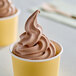 A yellow cup of chocolate soft serve ice cream.