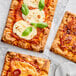 Three square pizzas topped with cheese, basil, and tomato sauce on a table.