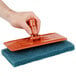 A hand holding a 3M Doodlebug blue scrub pad.