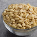 A glass bowl filled with blanched peanuts on a gray surface.