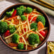 A bowl of rice topped with bamboo shoot strips, broccoli, carrots, and red bell peppers.