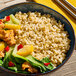 A bowl of cooked medium grain brown rice served with vegetables and pieces of tofu or chicken.