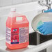 A person in blue gloves holding a gallon of pink Clean Quick Quaternary Sanitizer.