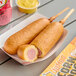 A tray of Foster Farms Honey Chicken Whole Grain Corn Dogs with a pink label on a stick.