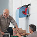 A man holding a Tork red and smoke wall mount wiper roll dispenser box.