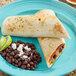 A plate with two large flour tortillas filled with assorted ingredients, served with black beans topped with cheese and lime wedges.