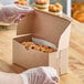 A person in gloves holding a Baker's Lane Kraft cupcake box filled with muffins.