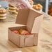 A hand holding a Baker's Lane Kraft bakery box of colorful macarons.