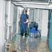 A man in blue work clothes using a Nilfisk wet/dry vacuum to clean a flooded floor.