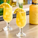 Two glasses of yellow liquid with pineapple slices and green leaves on the side.