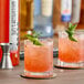 A glass of pink liquid with a lime garnish next to a bottle of SHOTT Watermelon and Lime Real Fruit Flavoring Syrup.