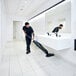 A man using a Nilfisk Dryft walk-behind floor scrubber with a lithium-ion battery to clean a bathroom.