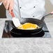 A chef using a Tablecraft countertop induction range to cook eggs in a pan.