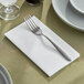 A fork and knife on a white linen-feel dinner napkin on a table.