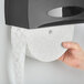 A hand holding a Scott Essential jumbo toilet paper roll.