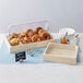 An American Metalcraft sun-bleached mango wood crate holding a tray of bagels and muffins on a table in a bakery display.