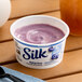 A plastic container of Silk blueberry soymilk yogurt alternative on a table.