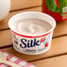 A container of Silk strawberry soymilk yogurt alternative on a table with a wooden spoon.