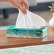 A hand pulling a white tissue from a Kleenex box on a table.