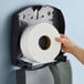A hand holding a Scott Essential jumbo roll of toilet paper.