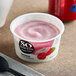 A close-up of a So Delicious Dairy-Free Raspberry Coconut Milk Yogurt cup with a black spoon inside.