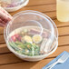 A hand putting a Dart clear plastic dome lid on a salad bowl.
