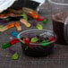 A clear plastic cup filled with gummy worms next to a clear plastic container of chocolate.