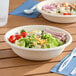 Two Dart ProPlanet compostable fiber take-out bowls filled with salad on a table.