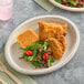 A Dart ProPlanet oval fiber platter with fried chicken and salad on a table with a wooden fork.