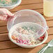 A hand using a Dart clear plastic lid on a bowl of food.