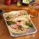 A tray of tacos with vegetables and meat on a table with a glass of amber liquid with ice and a straw.