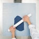 A person rolling out white fondant on a white Ateco silicone baking mat.