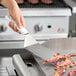 A person using a Choice square edge turner to flip bacon on a grill.