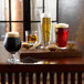 A wooden table with three glasses of dark beer and a bag of Briess Black Malt.