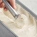 A hand scooping brown butter gelato with a silver scoop.