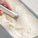 A hand scooping Bravo Gelato vanilla bean gelato with a metal scoop.