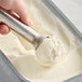 A hand scooping Bravo Gelato Fior di Latte into a metal pan.