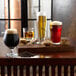 A wooden table with three glasses of different types of beer and a bag of Briess White Wheat Malt