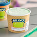A close-up of a Bravo Gelato Mint Chocolate Chip gelato cup on a table.