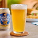 A glass of Samuel Adams Just the Haze Non-Alcoholic IPA next to a can of beer on a table outdoors.