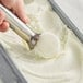A hand using a metal scoop to serve Bravo Gelato Limoncello sorbet into a metal pan.