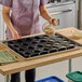 A woman pouring batter into a Sasa Demarle silicone cylinder mold with 24 holes.