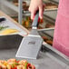 A stainless steel high heat solid beveled square edge turner with a nylon handle being used on a griddle.