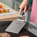 A stainless steel square edge turner with a black nylon handle being used on a grill.