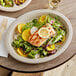 A plate of food with salmon and salad on a World Centric oval compostable fiber plate on a wood table.