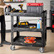 A man standing next to a black Rubbermaid utility cart with tools on it.
