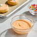A glass bowl filled with orange royal icing mix on a countertop near decorated cookies and sprinkles.