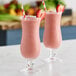Two glasses of pink strawberry smoothies with straws on a white background.