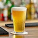 A glass of beer on a table with a coaster.