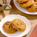 A plate of Otis Spunkmeyer Pumpkin Spice chocolate chip cookies on a table with a cup of coffee.